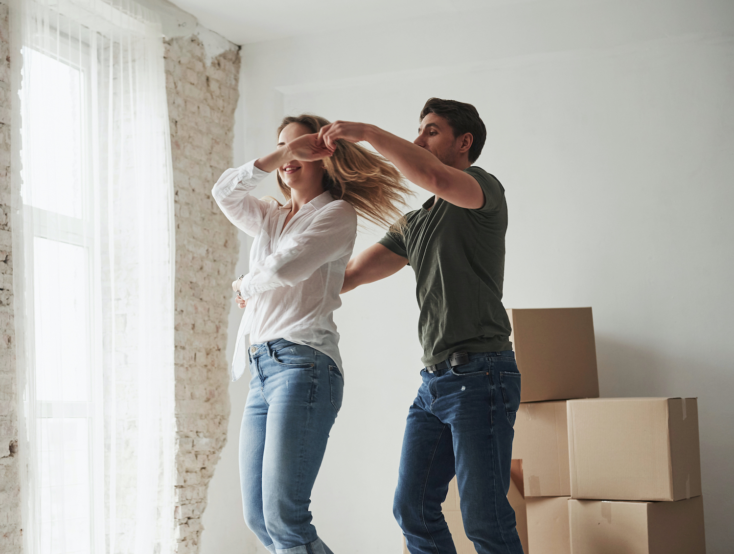 Young couple dancing in front of window first time home buyers